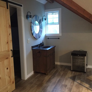 Mid-sized mountain style 3/4 medium tone wood floor and brown floor bathroom photo in Milwaukee with furniture-like cabinets, dark wood cabinets, a two-piece toilet, gray walls, an integrated sink and solid surface countertops