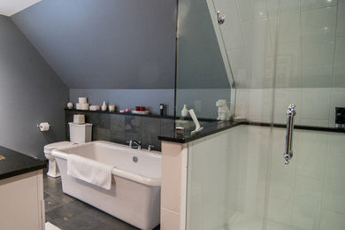 Photo of a medium sized contemporary ensuite bathroom in Milwaukee with a freestanding bath, a corner shower, a two-piece toilet, white tiles, ceramic tiles, grey walls, slate flooring, a submerged sink and engineered stone worktops.