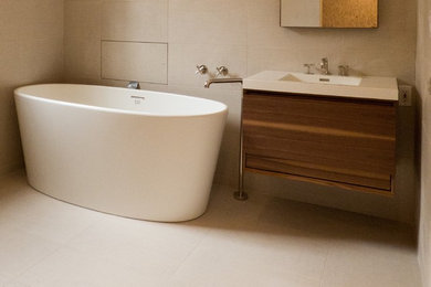 Freestanding bathtub - mid-sized modern master beige tile and porcelain tile freestanding bathtub idea in New York with a wall-mount sink, flat-panel cabinets, medium tone wood cabinets, beige walls and solid surface countertops