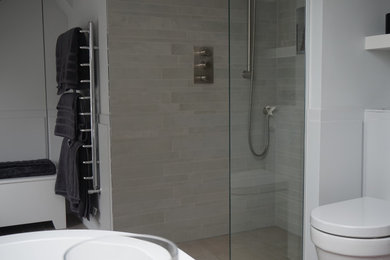 ロンドンにある高級な中くらいなコンテンポラリースタイルのおしゃれなマスターバスルーム (フラットパネル扉のキャビネット、グレーのキャビネット、置き型浴槽、オープン型シャワー、壁掛け式トイレ、ベージュのタイル、セラミックタイル、グレーの壁、セラミックタイルの床、コンソール型シンク、茶色い床、オープンシャワー) の写真