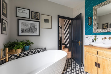 Medium sized classic family bathroom in London with light wood cabinets, a freestanding bath, a walk-in shower, a wall mounted toilet, multi-coloured tiles, ceramic tiles, multi-coloured walls, cement flooring, a vessel sink, wooden worktops, black floors, an open shower, a wall niche, a single sink and a freestanding vanity unit.