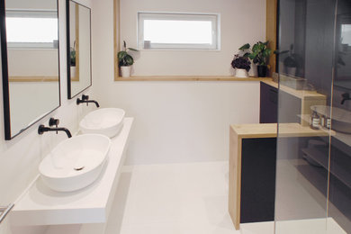This is an example of a large contemporary ensuite bathroom in Kent with freestanding cabinets, white cabinets, a walk-in shower, a wall mounted toilet, black and white tiles, stone slabs, white walls, slate flooring, a vessel sink, quartz worktops, white floors, an open shower and white worktops.