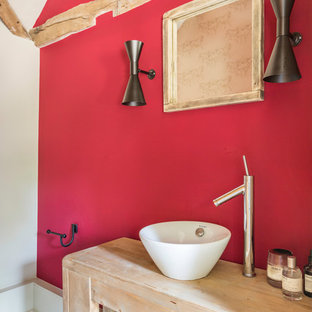 Rural bathroom with light wood cabinets, red walls, a vessel sink and grey floors.