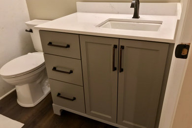 Alcove shower - mid-sized transitional kids' dark wood floor and brown floor alcove shower idea in Portland with flat-panel cabinets, gray cabinets, a two-piece toilet, beige walls, an undermount sink, quartz countertops, a hinged shower door and white countertops