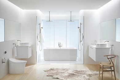 Exempel på ett mellanstort modernt en-suite badrum, med släta luckor, vita skåp, ett fristående badkar, en dusch/badkar-kombination, en toalettstol med hel cisternkåpa, vit kakel, porslinskakel, vita väggar, ljust trägolv, ett fristående handfat, bänkskiva i akrylsten, beiget golv och med dusch som är öppen