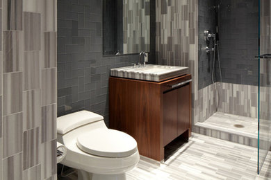 ワシントンD.C.にある小さなモダンスタイルのおしゃれな浴室 (フラットパネル扉のキャビネット、茶色いキャビネット、コーナー設置型シャワー、グレーのタイル、グレーの壁、オーバーカウンターシンク、グレーの床、開き戸のシャワー) の写真