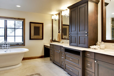 Photo of a large traditional ensuite bathroom in Louisville with raised-panel cabinets, dark wood cabinets, a freestanding bath, beige walls, porcelain flooring, a submerged sink, solid surface worktops and beige floors.