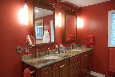 Modelo de cuarto de baño principal clásico de tamaño medio con armarios con paneles con relieve, puertas de armario de madera oscura, paredes rojas, lavabo bajoencimera y encimera de granito