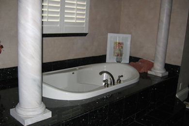Ejemplo de cuarto de baño principal clásico grande con bañera empotrada, baldosas y/o azulejos negros, losas de piedra y paredes beige