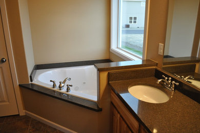 Example of a stone slab corner bathtub design in Seattle with an undermount sink and granite countertops