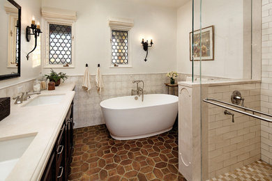 Photo of a small mediterranean ensuite bathroom in Santa Barbara with recessed-panel cabinets, dark wood cabinets, a freestanding bath, an alcove shower, multi-coloured tiles, ceramic tiles, white walls, a submerged sink, solid surface worktops, brown floors, a hinged door and terracotta flooring.