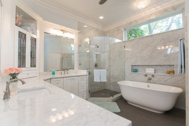 Photo of a large traditional ensuite bathroom in Dallas with glass-front cabinets, white cabinets, a freestanding bath, a corner shower, a one-piece toilet, white tiles, marble tiles, white walls, porcelain flooring, a submerged sink, marble worktops, grey floors, a hinged door and white worktops.