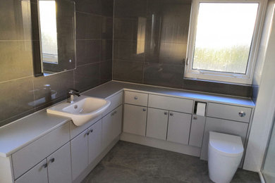 Inspiration for a large modern family bathroom in Edinburgh with flat-panel cabinets, grey cabinets, a double shower, a one-piece toilet, grey tiles, porcelain tiles, grey walls, porcelain flooring, a built-in sink, laminate worktops, grey floors, a sliding door and grey worktops.
