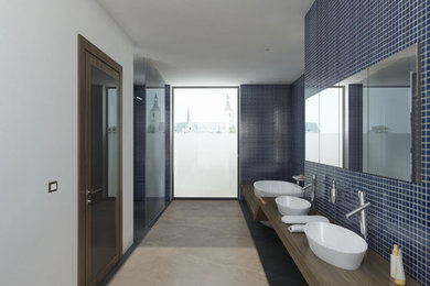 Photo of a medium sized ensuite bathroom in Amsterdam with a console sink, flat-panel cabinets, wooden worktops, a built-in bath, a walk-in shower, a one-piece toilet, blue tiles, ceramic tiles, white walls and concrete flooring.
