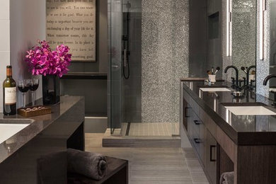 Пример оригинального дизайна: большая главная ванная комната в стиле модернизм с врезной раковиной, плоскими фасадами, темными деревянными фасадами, столешницей из искусственного кварца, полновстраиваемой ванной, угловым душем, серой плиткой и серыми стенами