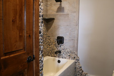 Réalisation d'une salle de bain principale tradition en bois brun de taille moyenne avec un combiné douche/baignoire, un carrelage marron, une plaque de galets, un mur gris, un sol en carrelage de porcelaine, un plan de toilette en granite et un sol noir.