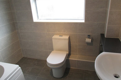 Idéer för ett mellanstort modernt badrum för barn, med släta luckor, grå skåp, en toalettstol med separat cisternkåpa, grå kakel, keramikplattor, grå väggar, klinkergolv i keramik och laminatbänkskiva