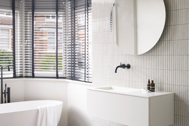 This is an example of a medium sized contemporary family bathroom in Other with a freestanding bath, white tiles, porcelain tiles, slate flooring, grey floors, flat-panel cabinets, white cabinets, white walls, an integrated sink and white worktops.