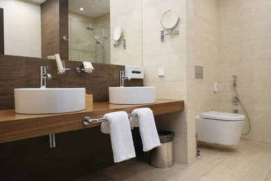 Example of a mid-sized trendy master dark wood floor alcove shower design in New York with open cabinets, light wood cabinets, a wall-mount toilet, beige walls, a vessel sink and wood countertops