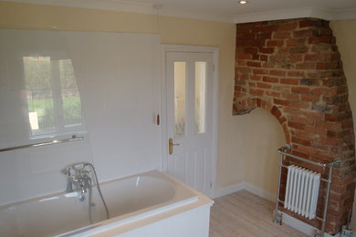 This is an example of a large rustic ensuite bathroom in Cambridgeshire with a pedestal sink, shaker cabinets, white cabinets, wooden worktops, a built-in bath, a shower/bath combination, a two-piece toilet, white tiles, ceramic tiles, green walls and lino flooring.