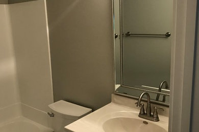 Inspiration pour une petite salle de bain design avec un placard à porte shaker, des portes de placard blanches, un mur gris, un sol en vinyl, un lavabo intégré, un plan de toilette en surface solide et un sol gris.