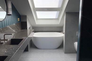 This is an example of a small scandi ensuite bathroom in London with open cabinets, grey cabinets, a freestanding bath, a walk-in shower, a wall mounted toilet, grey tiles, limestone tiles, blue walls, terrazzo flooring, a submerged sink, marble worktops, grey floors, a hinged door and grey worktops.