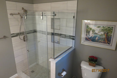 This is an example of a small traditional ensuite bathroom with raised-panel cabinets, white cabinets, an alcove shower, grey tiles, porcelain tiles, grey walls, porcelain flooring, an integrated sink, solid surface worktops, grey floors and a sliding door.