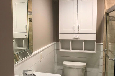 ワシントンD.C.にあるお手頃価格の小さなトランジショナルスタイルのおしゃれなバスルーム (浴槽なし) (落し込みパネル扉のキャビネット、白いキャビネット、アンダーマウント型浴槽、シャワー付き浴槽	、一体型トイレ	、ベージュのタイル、トラバーチンタイル、ベージュの壁、スレートの床、コンソール型シンク、ガラスの洗面台、茶色い床、引戸のシャワー、白い洗面カウンター、ニッチ、洗面台1つ、造り付け洗面台、羽目板の壁) の写真