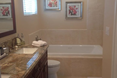 This is an example of a medium sized traditional ensuite bathroom in Los Angeles with dark wood cabinets, a built-in bath, beige tiles, porcelain tiles, beige walls, porcelain flooring, a submerged sink, granite worktops, beige floors, raised-panel cabinets and a one-piece toilet.