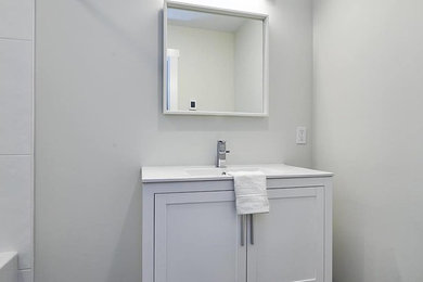 Mid-sized minimalist 3/4 porcelain tile and gray floor bathroom photo in Vancouver with shaker cabinets, white cabinets, gray walls, an undermount sink, solid surface countertops and white countertops