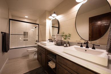 Photo of a medium sized farmhouse ensuite bathroom in Other with shaker cabinets, brown cabinets, an alcove bath, a shower/bath combination, a two-piece toilet, white tiles, metro tiles, beige walls, ceramic flooring, a vessel sink, quartz worktops, beige floors, a sliding door and white worktops.