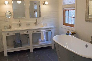 Diseño de cuarto de baño campestre con puertas de armario blancas, bañera exenta, paredes blancas, suelo de pizarra, lavabo de seno grande, encimera de mármol, suelo gris y encimeras blancas