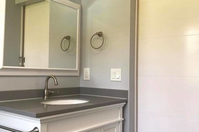 Mid-sized transitional 3/4 white tile and porcelain tile medium tone wood floor and brown floor bathroom photo in New York with recessed-panel cabinets, white cabinets, a two-piece toilet, gray walls, an undermount sink, solid surface countertops and gray countertops