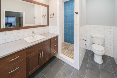 Example of a mid-sized minimalist master white tile and porcelain tile porcelain tile and black floor bathroom design in St Louis with shaker cabinets, brown cabinets, a two-piece toilet, gray walls, a drop-in sink, quartzite countertops and gray countertops