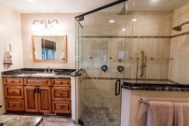Corner shower - mid-sized traditional 3/4 beige tile and porcelain tile porcelain tile and gray floor corner shower idea in Detroit with raised-panel cabinets, medium tone wood cabinets, beige walls, an undermount sink, quartz countertops, a hinged shower door and black countertops
