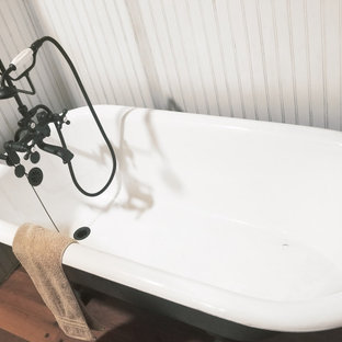 Modelo de cuarto de baño principal y panelado, rústico, de tamaño medio, panelado, con armarios tipo mueble, puertas de armario de madera oscura, bañera con patas, combinación de ducha y bañera, sanitario de dos piezas, paredes amarillas, suelo de madera en tonos medios, lavabo encastrado, encimera de madera, suelo marrón, ducha con cortina, encimeras marrones y panelado