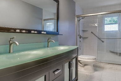 ニューヨークにある中くらいなトランジショナルスタイルのおしゃれなバスルーム (浴槽なし) (ガラス扉のキャビネット、濃色木目調キャビネット、アルコーブ型シャワー、一体型トイレ	、グレーの壁、大理石の床、一体型シンク、ガラスの洗面台) の写真
