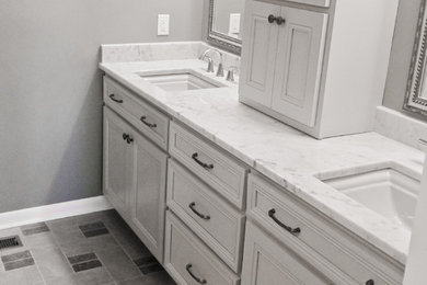 Inredning av ett modernt en-suite badrum, med ett undermonterad handfat, släta luckor, grå skåp, marmorbänkskiva, grå kakel, grå väggar och mosaikgolv