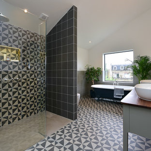 Photo of a large modern bathroom in London with grey cabinets, a claw-foot bath, beige tiles, black tiles, cement tiles, white walls, cement flooring, a vessel sink, wooden worktops, multi-coloured floors and brown worktops.