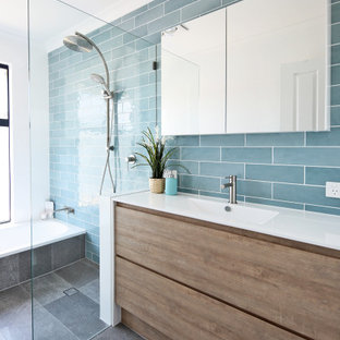 Inspiration for a beach style wet room bathroom in Perth with flat-panel cabinets, medium wood cabinets, an alcove tub, blue tile, an integrated sink, grey floor, an open shower and white benchtops.