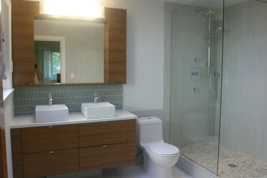 Modern inredning av ett badrum, med ett fristående handfat, släta luckor, skåp i mellenmörkt trä, bänkskiva i kvarts, ett platsbyggt badkar, en öppen dusch, en toalettstol med hel cisternkåpa och grön kakel