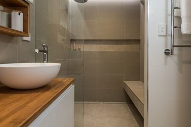 Idéer för att renovera ett mellanstort funkis brun brunt en-suite badrum, med vita skåp, en dubbeldusch, en vägghängd toalettstol, grå kakel, porslinskakel, klinkergolv i porslin, träbänkskiva, grått golv och med dusch som är öppen