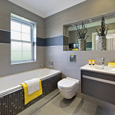 Example of a trendy gray tile drop-in bathtub design in Perth with an integrated sink, flat-panel cabinets, a wall-mount toilet and gray walls
