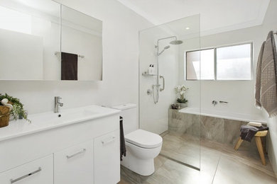 Exempel på ett mellanstort modernt badrum, med släta luckor, vita skåp, ett badkar i en alkov, en öppen dusch, en toalettstol med separat cisternkåpa, beige kakel, keramikplattor, vita väggar, klinkergolv i keramik, ett avlångt handfat och bänkskiva i akrylsten