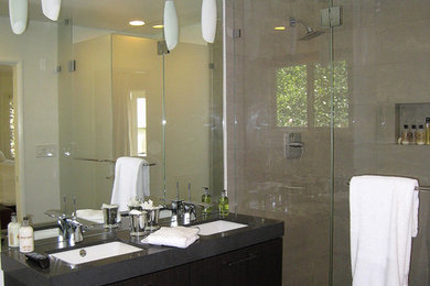 Cette photo montre une salle de bain principale tendance en bois foncé de taille moyenne avec un lavabo encastré, un placard à porte plane, un plan de toilette en surface solide, une baignoire encastrée, une douche d'angle, un carrelage gris, des carreaux de porcelaine, un mur gris et un sol en carrelage de porcelaine.