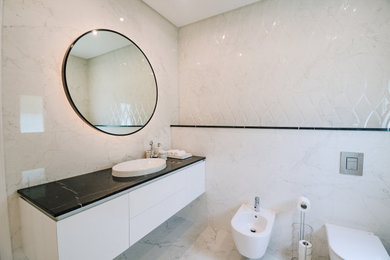 Inspiration for a mid-sized transitional white tile and porcelain tile porcelain tile, white floor and single-sink corner shower remodel in Other with a bidet, white walls, an integrated sink, marble countertops, a hinged shower door and black countertops
