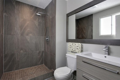 カルガリーにある高級な中くらいなコンテンポラリースタイルのおしゃれなバスルーム (浴槽なし) (フラットパネル扉のキャビネット、グレーのキャビネット、アルコーブ型シャワー、分離型トイレ、茶色いタイル、グレーのタイル、石タイル、グレーの壁、一体型シンク、人工大理石カウンター) の写真