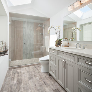 Inspiration for a mid-sized transitional master bathroom in Vancouver with an undermount sink, recessed-panel cabinets, grey cabinets, engineered quartz benchtops, an alcove shower, a bidet, gray tile, porcelain tile, porcelain floors, white walls, brown floor and a hinged shower door.