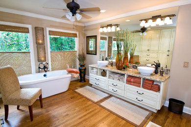 他の地域にあるトランジショナルスタイルのおしゃれなマスターバスルーム (ベッセル式洗面器、御影石の洗面台、置き型浴槽、ベージュの壁、無垢フローリング) の写真