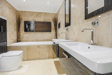 Expansive modern ensuite bathroom in Essex with glass-front cabinets, black cabinets, a built-in bath, a one-piece toilet, travertine tiles, beige walls, travertine flooring, a wall-mounted sink, beige floors and white worktops.